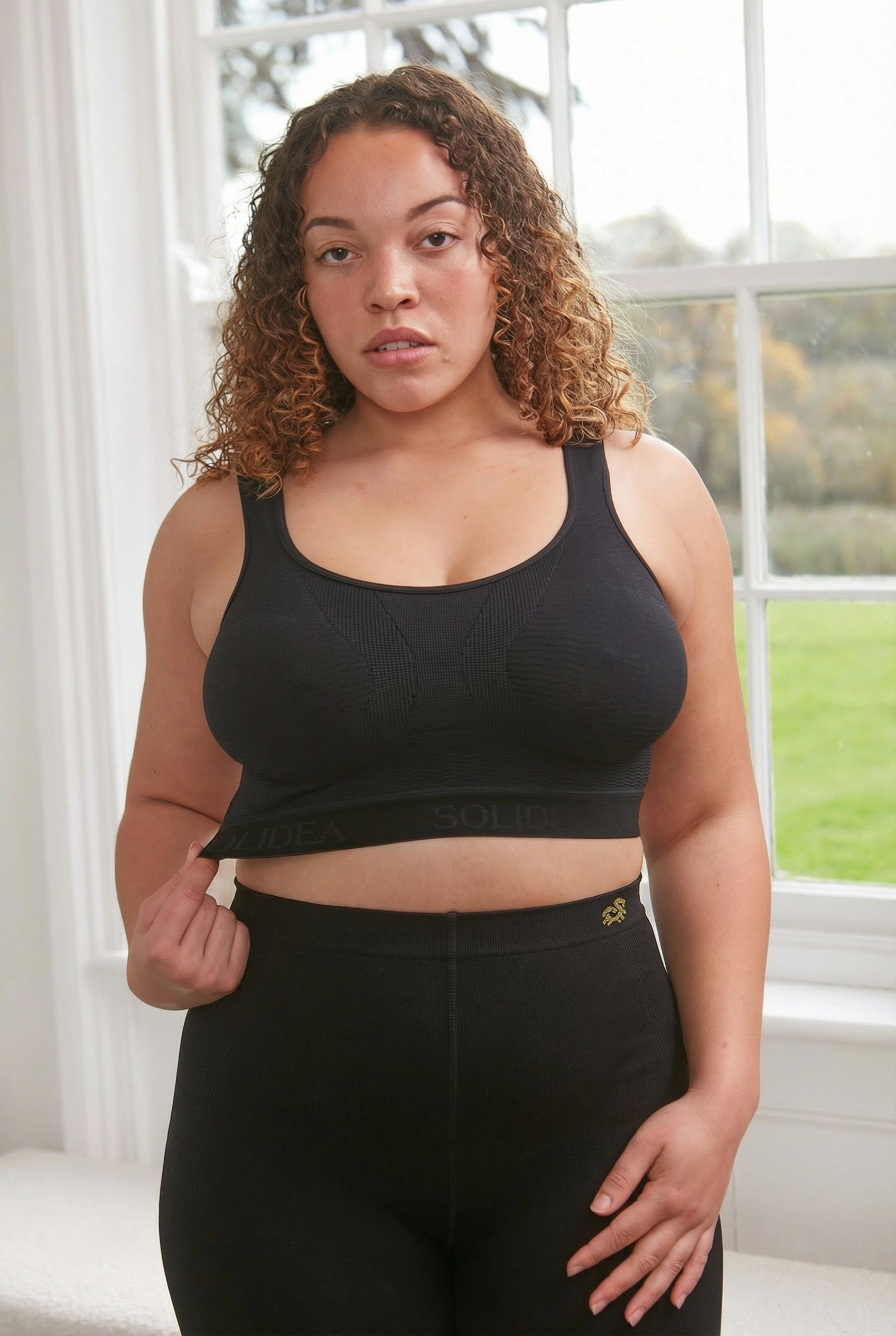 A woman standing by a window wearing the Silver Wave Skin Compression Bra in Nero